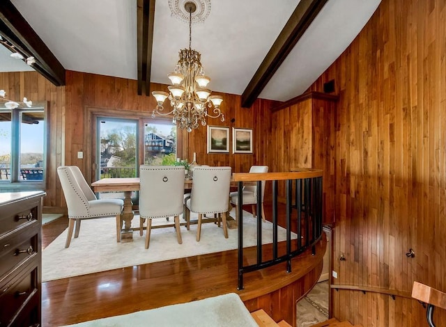 dining space with wood walls, a chandelier, beamed ceiling, and wood finished floors