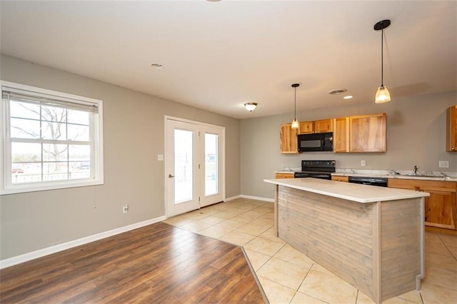 kitchen featuring black appliances, light wood-style flooring, decorative light fixtures, light countertops, and baseboards