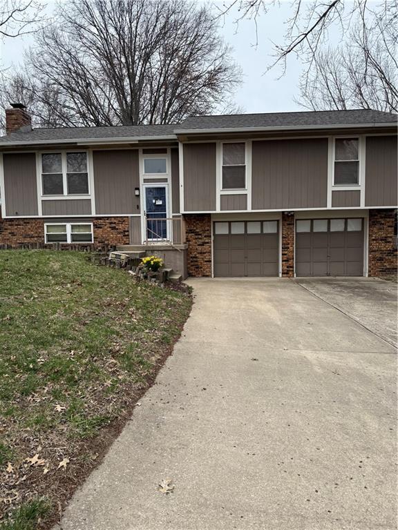 505 SE Sherri Ln, Blue Springs, MO 64014 - view of front of house featuring an attached garage, driveway, brick siding, and a chimney