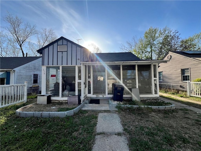 back of house with board and batten siding, fence, and a sunroom