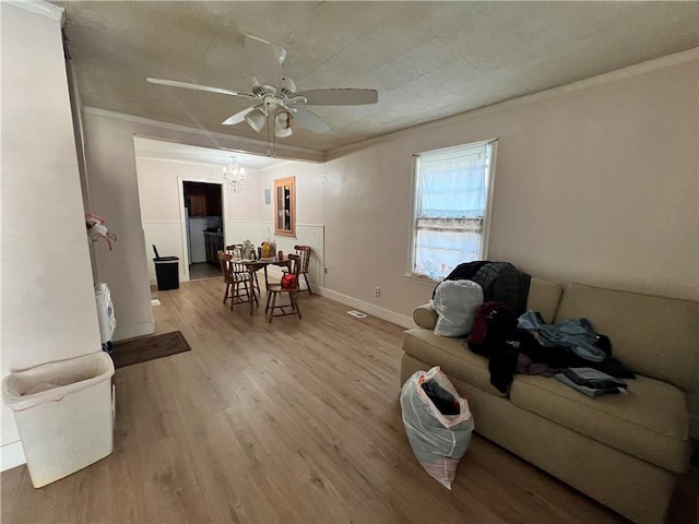 living room with crown molding, ceiling fan with notable chandelier, baseboards, and light wood-type flooring