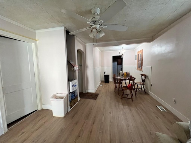 dining room with ceiling fan with notable chandelier, arched walkways, ornamental molding, visible vents, and wood finished floors