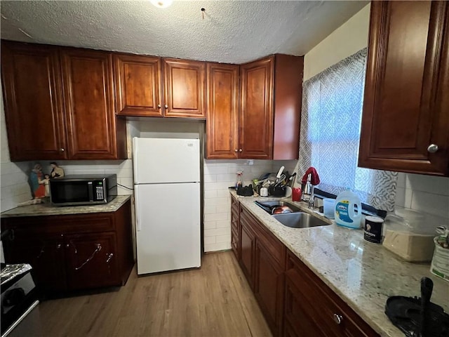 kitchen with light stone counters, a textured ceiling, freestanding refrigerator, light wood-style floors, and a sink
