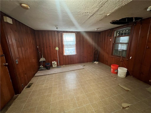 interior space with tile patterned floors, wood walls, visible vents, and a textured ceiling