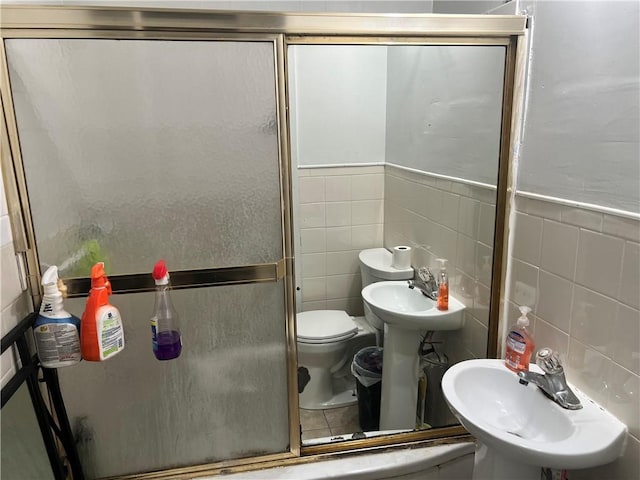 bathroom featuring toilet, tile walls, a sink, and a stall shower
