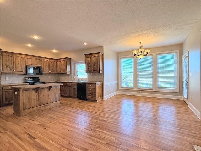 kitchen featuring light wood finished floors, a center island, a chandelier, black appliances, and a sink