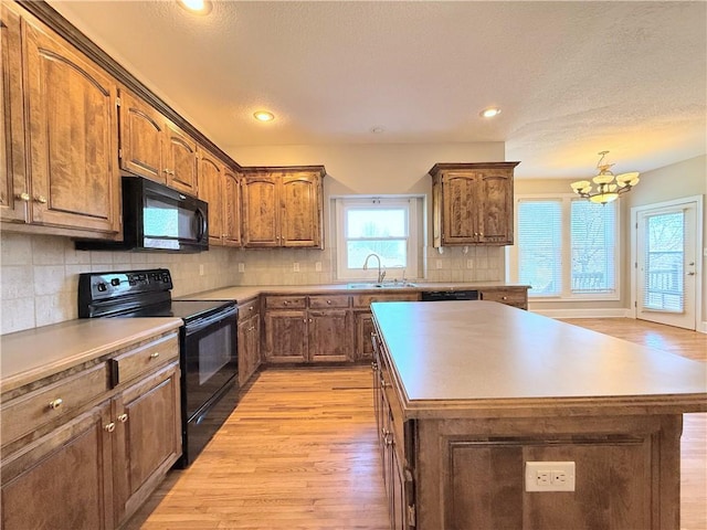 kitchen featuring a kitchen island, light wood-type flooring, an inviting chandelier, black appliances, and a sink