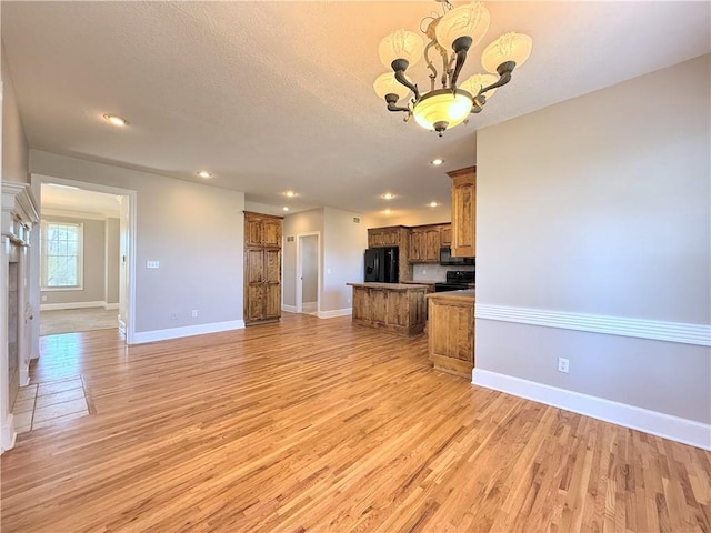 kitchen with black appliances, brown cabinetry, open floor plan, and a chandelier