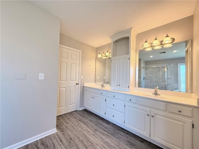 bathroom featuring wood finished floors, baseboards, double vanity, a sink, and a shower stall