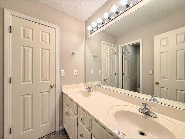 full bathroom featuring double vanity, a textured ceiling, toilet, and a sink