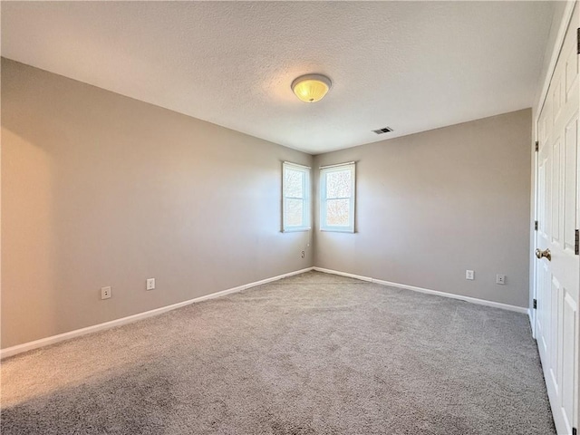 carpeted spare room featuring visible vents, baseboards, and a textured ceiling
