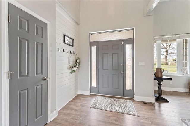 foyer entrance featuring wood finished floors, a high ceiling, baseboards, and visible vents