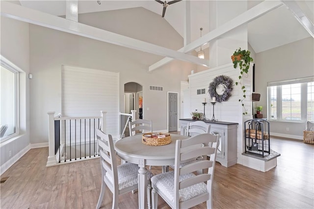 dining space featuring light wood finished floors, arched walkways, high vaulted ceiling, and a healthy amount of sunlight