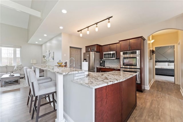 kitchen featuring arched walkways, wood finished floors, stainless steel appliances, and a breakfast bar