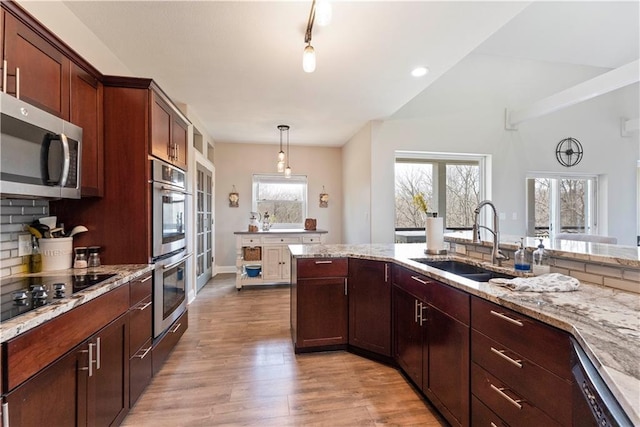 kitchen featuring a sink, decorative light fixtures, light stone countertops, light wood-style flooring, and appliances with stainless steel finishes