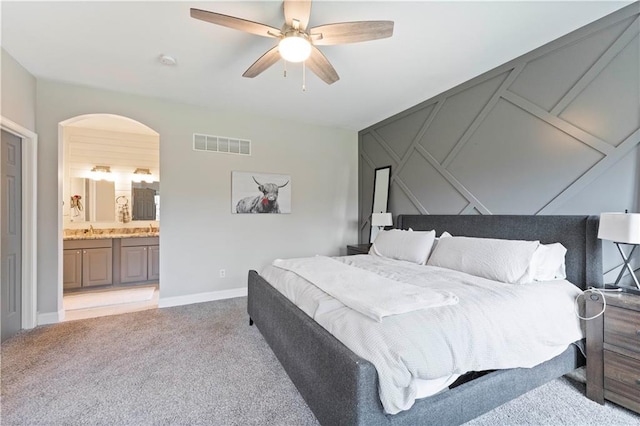 bedroom featuring a sink, arched walkways, visible vents, light colored carpet, and a decorative wall
