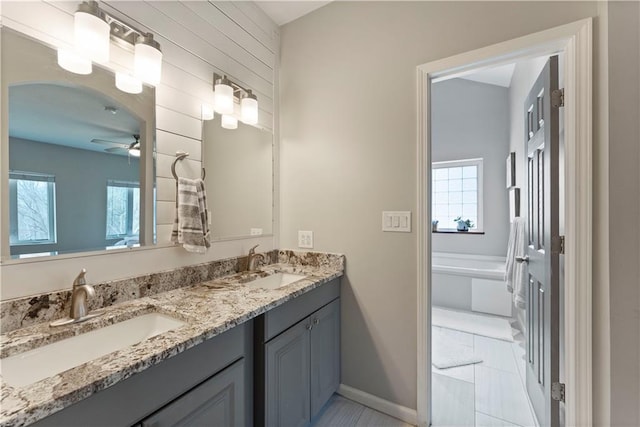 full bathroom with double vanity, a ceiling fan, baseboards, and a sink