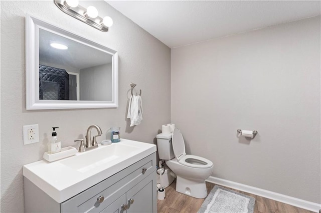 bathroom featuring toilet, vanity, wood finished floors, and baseboards