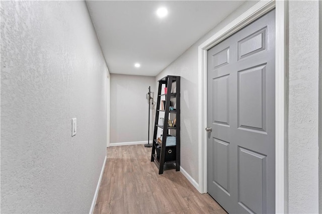 corridor featuring baseboards, a textured wall, wood finished floors, and recessed lighting