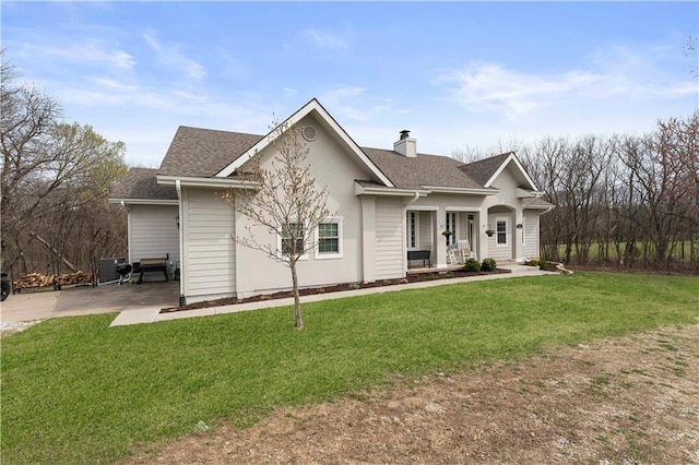 ranch-style house featuring a chimney, a front lawn, roof with shingles, and covered porch