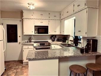 kitchen featuring stainless steel range with electric stovetop, stone finish floor, a sink, freestanding refrigerator, and black microwave