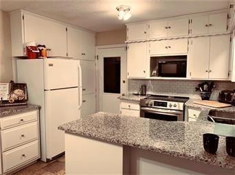 kitchen featuring backsplash, freestanding refrigerator, black microwave, stainless steel range with electric cooktop, and a peninsula
