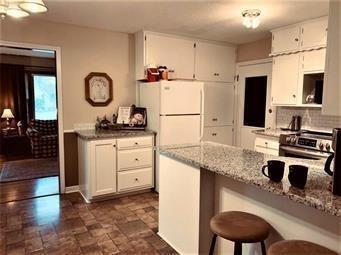 kitchen with stainless steel range with electric stovetop, a peninsula, stone finish flooring, white cabinetry, and light stone counters