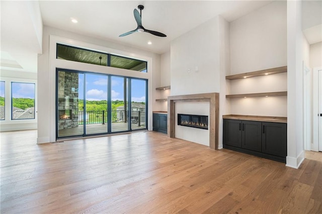 2317 SW Morris Dr, Lees Summit, MO 64082 - unfurnished living room featuring a glass covered fireplace, light wood-style floors, a ceiling fan, a high ceiling, and recessed lighting