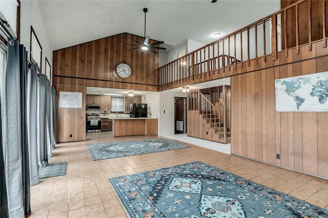 134 Timber Valley Dr, Linn Valley, KS 66040 - unfurnished living room with ceiling fan, high vaulted ceiling, wood walls, stairs, and light tile patterned floors