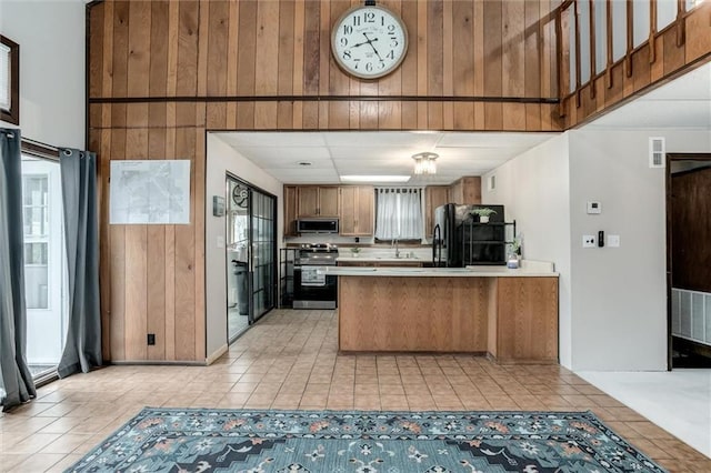 134 Timber Valley Dr, Linn Valley, KS 66040 - kitchen with a peninsula, wooden walls, light countertops, appliances with stainless steel finishes, and light tile patterned floors