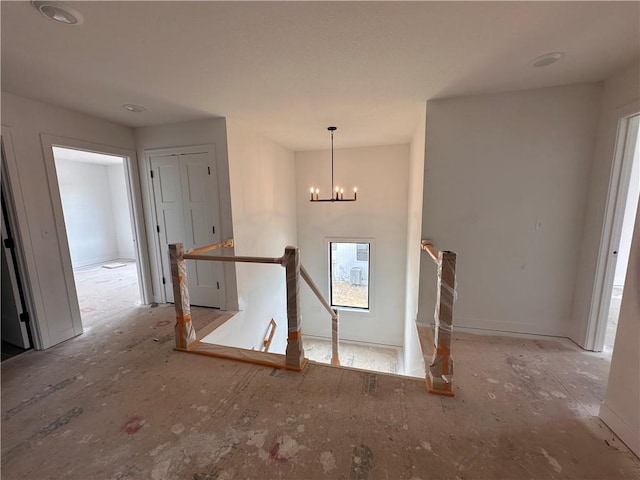 corridor with an upstairs landing and an inviting chandelier