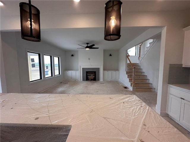 unfurnished living room with ceiling fan, stairway, and a fireplace