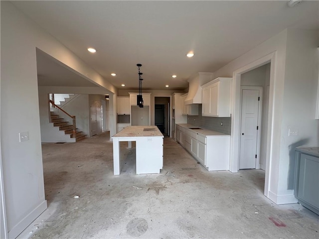 kitchen with tasteful backsplash, a center island, cooktop, white cabinetry, and custom range hood