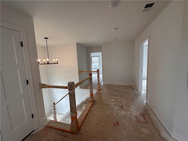 hallway with baseboards, visible vents, a notable chandelier, and an upstairs landing