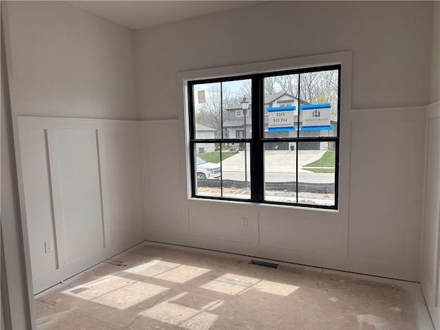 unfurnished room featuring a decorative wall, visible vents, and wainscoting
