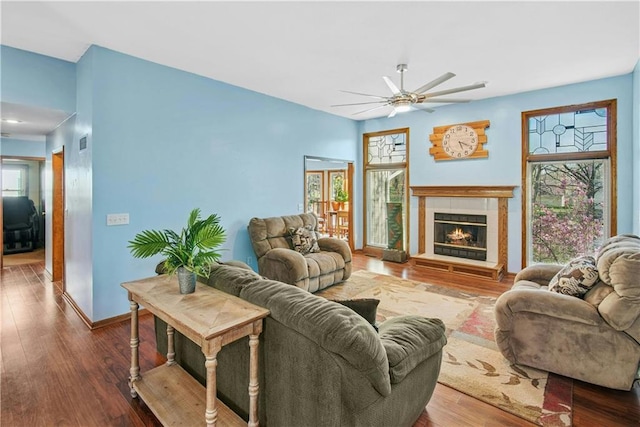 living area with baseboards, visible vents, ceiling fan, a tile fireplace, and wood finished floors
