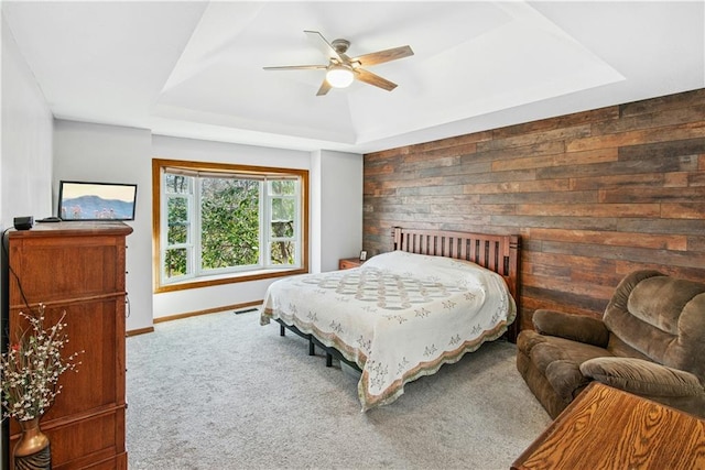 carpeted bedroom featuring ceiling fan, visible vents, wood walls, a raised ceiling, and baseboards