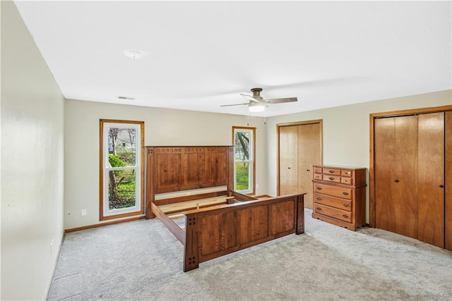 bedroom with light carpet, a ceiling fan, visible vents, and multiple closets