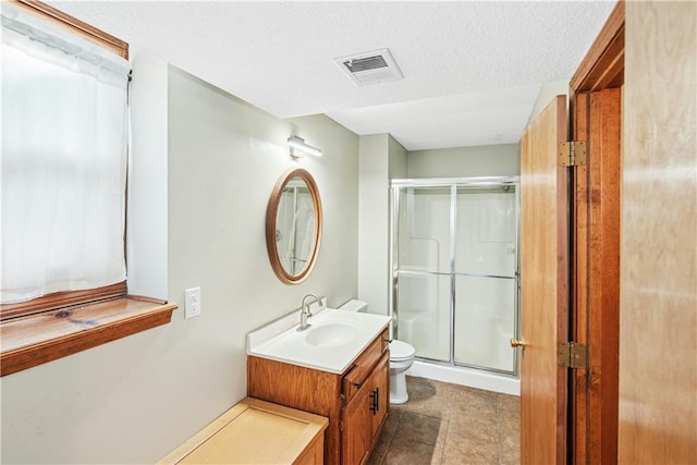 bathroom with visible vents, toilet, a textured ceiling, vanity, and a stall shower