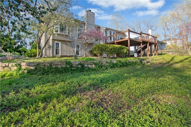 rear view of property with a wooden deck, stairs, a lawn, and a chimney