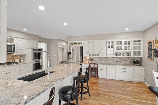 kitchen featuring a sink, light wood-type flooring, appliances with stainless steel finishes, white cabinetry, and backsplash