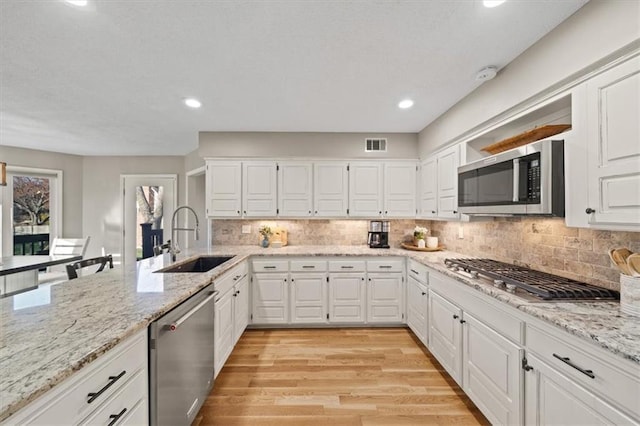kitchen with visible vents, white cabinets, a sink, light wood-type flooring, and stainless steel appliances