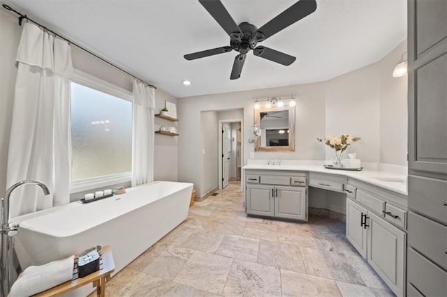 bathroom with double vanity, stone finish flooring, a ceiling fan, a freestanding bath, and a sink
