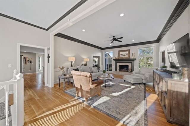 living area featuring a fireplace with raised hearth, ceiling fan, crown molding, recessed lighting, and wood finished floors