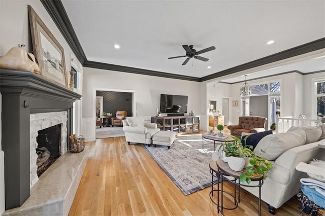 living area featuring light wood-style floors, a stone fireplace, ornamental molding, and a ceiling fan