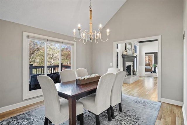 dining area featuring baseboards, light wood-type flooring, a chandelier, a fireplace with raised hearth, and high vaulted ceiling