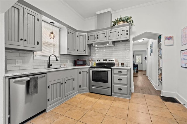 kitchen with ornamental molding, gray cabinets, light tile patterned floors, stainless steel appliances, and a sink