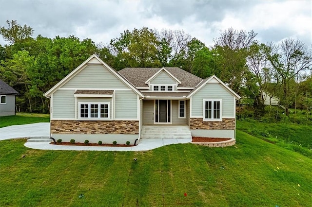 rear view of house featuring a lawn, a porch, stone siding, and roof with shingles