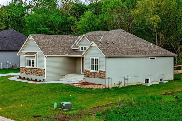 view of front of property with roof with shingles, a front yard, and stone siding
