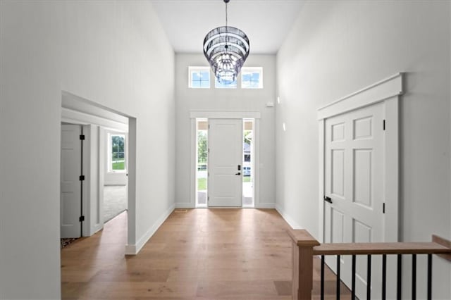 foyer entrance with a high ceiling, a notable chandelier, plenty of natural light, and wood finished floors